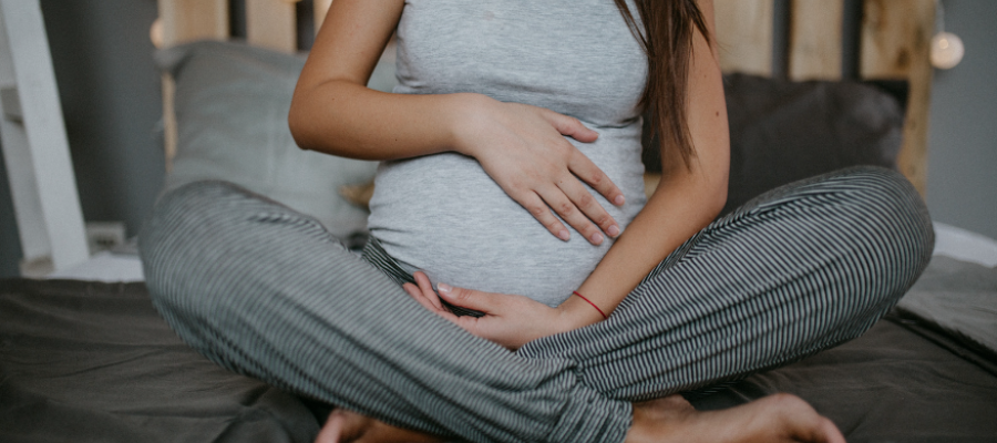 pregnant woman holding her bump, whilst sitting on a bed.