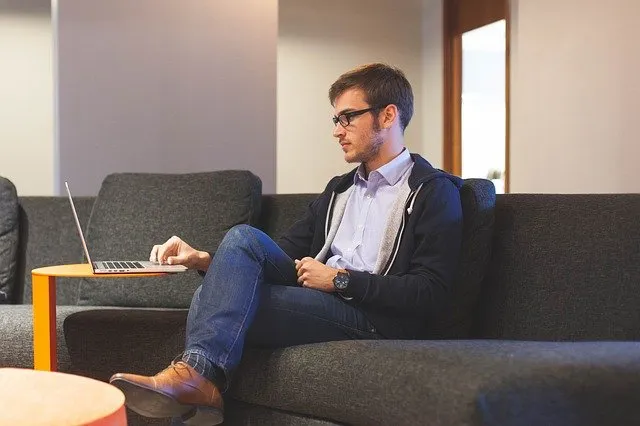 Man sat on grey sofa, laptop on table, his hand resting on the laptop