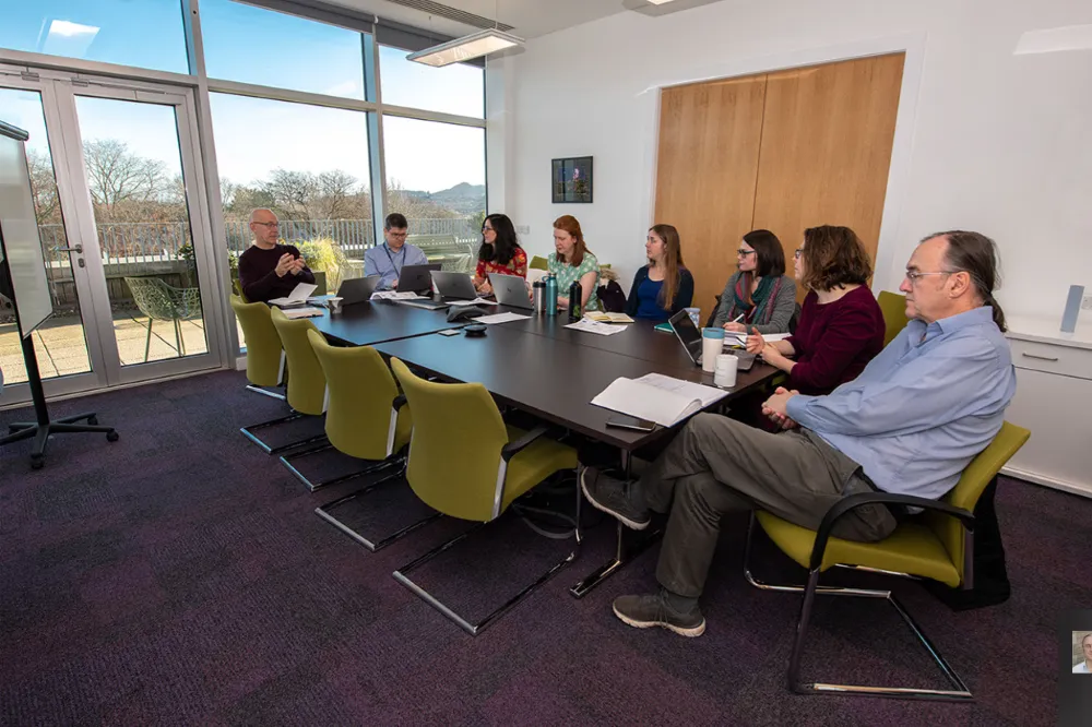 8 memners of the Generation Scotland team sat around a meeting table in discussion.