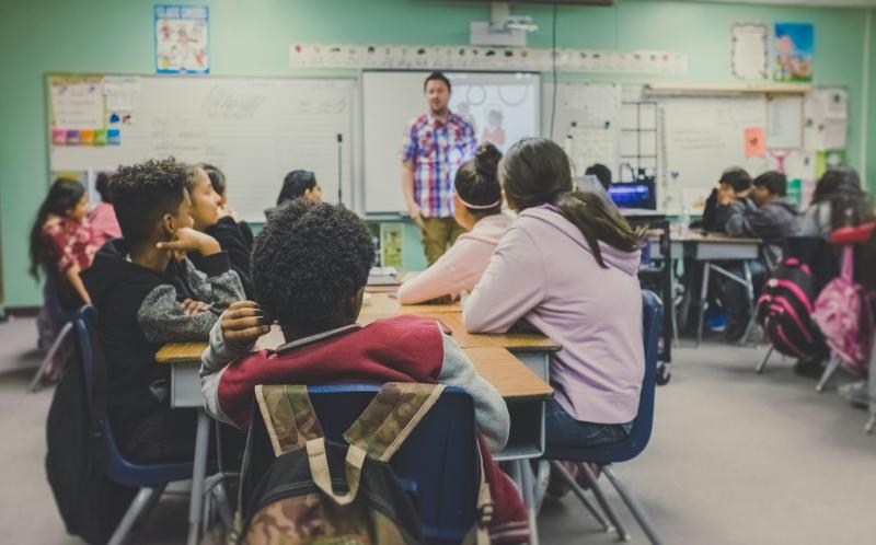 Young people studying in a classroom with a teacher at the front of the room